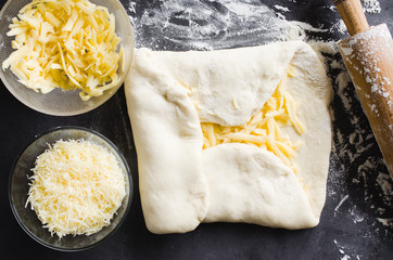 Rolled dough, baking flour, grated cheese and rolling pin on a dark blackboard.