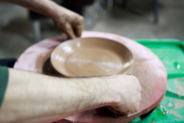 a master ceramist made plate from red clay on a potter's wheel, on a sheet of particle board for better removal and further drying. before removed chipboard he cuts plate off with a string. reportage.