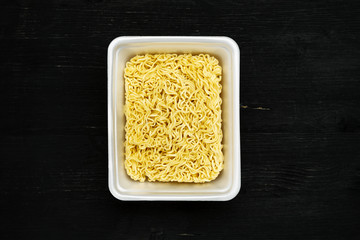 Instant noodles in container on a black wooden table, top view