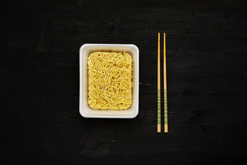 Instant noodles in container with chopsticks on a black wooden table, top view