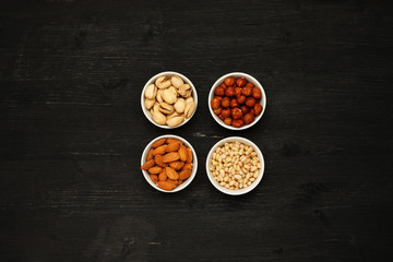 Different nuts in ceramic bowls on a black wooden table, top viev