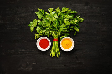 Bunch of green fresh parsley with spices in white ceramic bowls on a black wooden table, top view