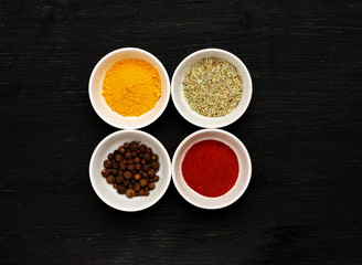 Different spices in ceramic bowls on a black wooden table, top view