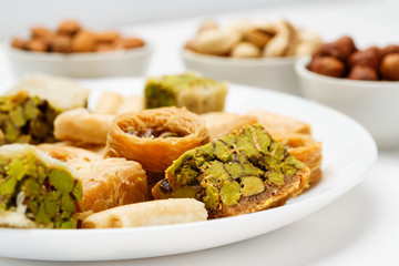 Traditional oriental sweets in white plate with different nuts on a white table, side view, close-up