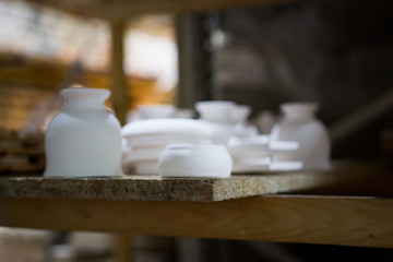 articles of clay made by slip forming using plaster molds a master with 13 years of experience. drying on a rack with shelves from chipboard. sockets, glasses, plates.