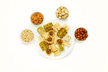 Traditional oriental sweets in white plate with different nuts on a white table, top view