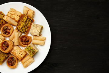 Traditional oriental sweets in white plate with different nuts on a black table, top view, copy space