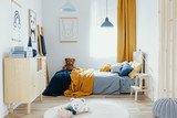 Teddy bear on single wooden bed in blue and orange bedroom interior