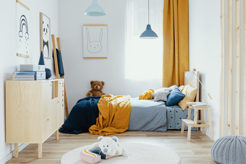 Teddy bear on single wooden bed in blue and orange bedroom interior
