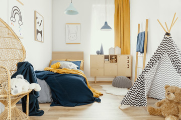 Stylish wooden commode in bright bedroom interior with poster on the wall