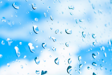 Water drops after rain on clean glass. Beautiful drops texture. Background of drops on the glass with blue sky and clouds