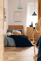 Wicker peacock chair in bright kid's bedroom interior with wooden furniture