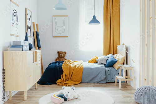 Teddy bear on single wooden bed in blue and orange bedroom interior
