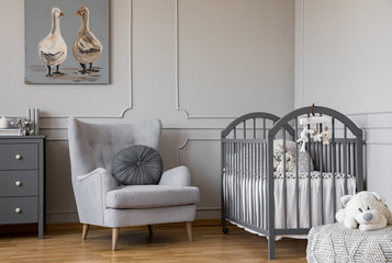 Ducks on cute oil painting in tasteful baby room with grey armchair and wooden crib, copy space on empty wall