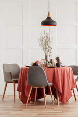 Dry flowers in vase on dining table covered with dark orange tablecloth