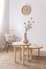 Cotton flower in beige vase on small wooden coffee table next to wicker chair with pillow