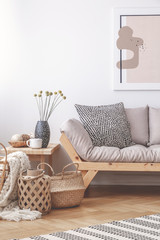 Straw basket next to comfortable settee and table in elegant living room interior, real photo