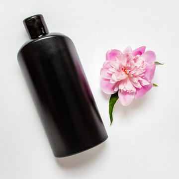 Black shapoo bottle with pink peony flower on white background