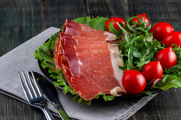 Plate with sliced jamon, tomatoes and herbs on a wooden table