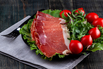 Plate with sliced jamon, tomatoes and herbs on a wooden table