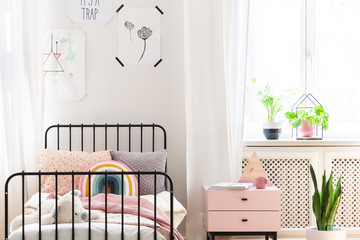 Bright child bedroom with colorful bedding, prints on the wall and pastel pink bedside table, real photo