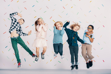 Girls and boys having fun while jumping against colorful wallpaper. Friends in the school