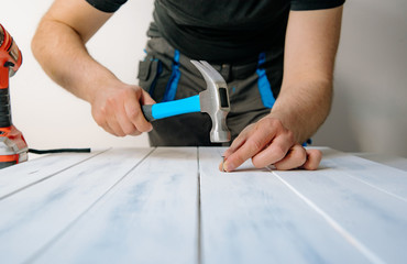 A man nails a nail with a hammer to a wooden board. The concept of DIY and renovation of new things. A man tinkering at home, working with wood.