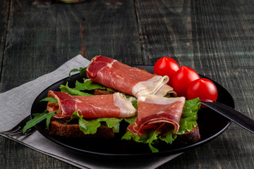 On the table there is a dish with jamon sandwiches, tomato and greens