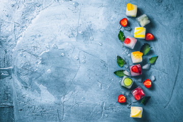 Ice cubes with fruit and broken ice on a stone blue background with mint leaves and fresh fruit. Mint, strawberry, cherry, lemon, orange. Flat lay, top view