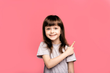 Portrait of puzzled brunet little girl kid with dark hair wears casual grey t shirt, points with...