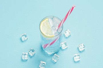 Glass of water or drink with ice and lemon on a blue background with ice cubes. Concept of a hot summer, alcohol, cooling drink, quenching thirst. Flat lay, top view