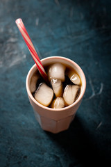 Iced coffee in a glass on a dark blue stone background. Concept cooling drink, thirst, summer, cola with ice. Flatlay, top view