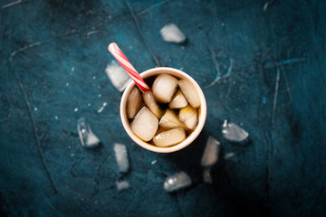 Iced coffee in a glass on a dark blue stone background with ice cubes. Concept cooling drink, thirst, summer, cola with ice, nightlife, club. Flat lay, top view