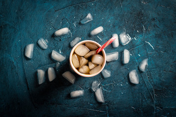 Iced coffee in a glass on a dark blue stone background with ice cubes. Concept cooling drink, thirst, summer, cola with ice, nightlife, club. Flat lay, top view