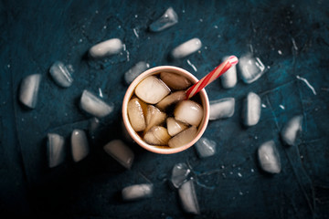 Iced coffee in a glass on a dark blue stone background with ice cubes. Concept cooling drink, thirst, summer, cola with ice, nightlife, club. Flat lay, top view