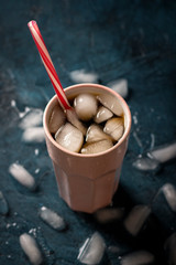 Iced coffee in a glass on a dark blue stone background with ice cubes. Concept cooling drink, thirst, summer, cola with ice, nightlife, club. Flat lay, top view