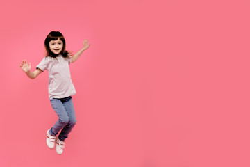 Little funny child girl jumping on a colored pink background. Happy and joyful, dancing and smiling, enjoy moment. Having fun
