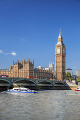 Big Ben and Houses of Parliament with red buses against boat in London, England, UK
