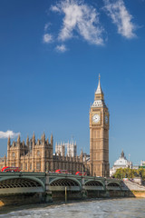 Big Ben and Houses of Parliament with red buses against boat in London, England, UK