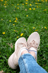Female crossed legs in light-colored sneakers and light jeans against the background of green grass