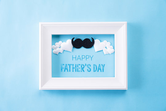 Happy fathers day concept. Top view of white picture frame with Happy father's day text on bright blue pastel background. Flat lay.
