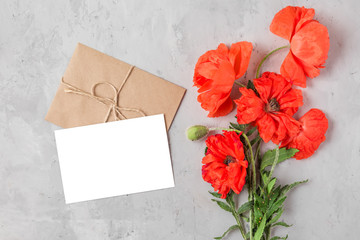 blank greeting card and envelope with red poppy flowers bouquet on concrete background. flat lay. mock up
