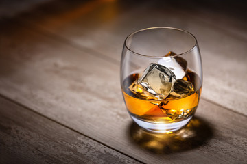 Whiskey, Bourbon, Rum, Cognac liquor with ice in a round rocking tumbler glass, on vintage rustic wooden table