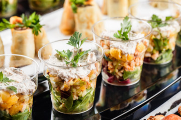 Delicious appetizers with salmon, shrimp, cheese and greens in glass cups on banquet table. Gourmet...