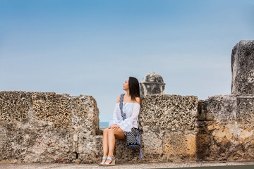 Fototapeta na wymiar Beautiful woman on white dress sitting alone at the walls surrounding the colonial city of Cartagena de Indias