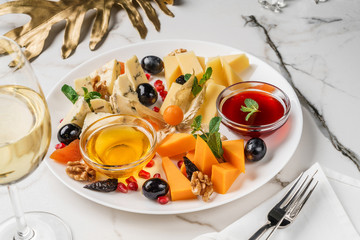 Cheese plate served with wine, nuts and honey over light marble background. Snacks and Wine appetizers set, top view, flat lay