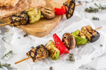 Grilled vegetable kebabs on skewers with zucchini, pepper, mushrooms, squash and herbs on paper...