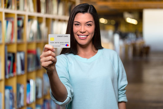 Smiling college university student holding mockup new bank credit card in library to assist her through education