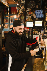 smiling barman pouring beer in a bar. Bearded courageous man pours you a foaming drink. Golden tap for draft beer.