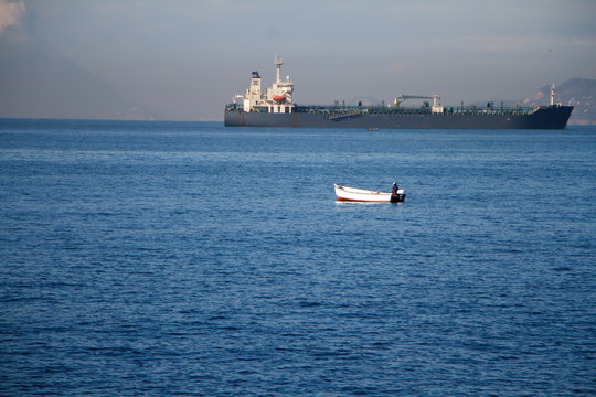 Unrecognizable man sailing on a boat with oars in the sea, a fisherman in a boat over a huge liner - Powered by Adobe